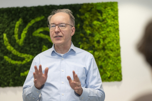 A male teacher wearing eyeglasses engaged in a conversation, set against a vibrant green background.