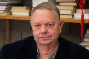 Seasoned man wearing a navy jacket, seated in an office with bookshelves behind him.