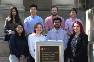 Group photo featuring eight individuals arranged in two rows, all smiling and posed for a formal group portrait.