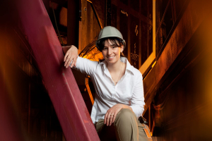 Woman sits in a construction site wearing a hard hat.