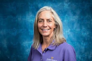 Janet Marnae stands against a blue background and smiles at the camera.