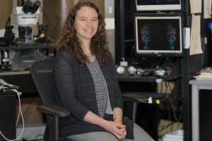 Image of professor sitting in her lab surrounded by equipment.
