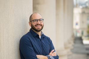 Kevin Hunter stands outside of Mellon Institute and leans against one of the pillars. He smiles at the camera.