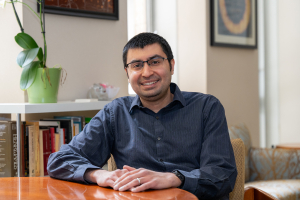 Saurabh Vyas sits at a wooden table in an office. He smiles at the camera.