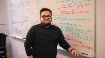 Gabe Gomes stands in front of a whiteboard with writing all over it.
