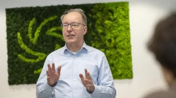 A male teacher wearing eyeglasses engaged in a conversation, set against a vibrant green background.