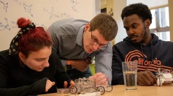 A picture of three people looking at a transparent car that is about 8 inches long and 6 inches tall.