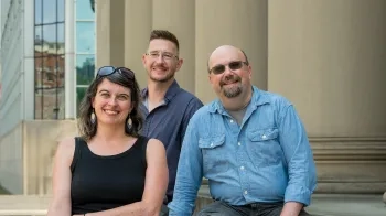 Image of two men and a woman on the steps of a building with large columns.